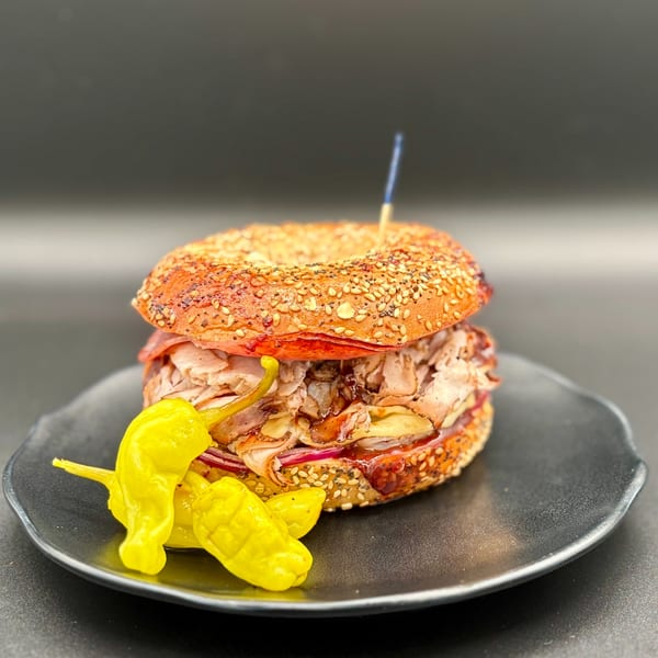 A Harvest deli sandwich on an everything bagel with meat, cheese, and red onion, served with yellow peppers.
