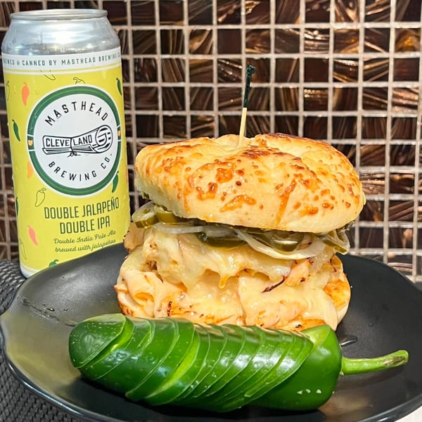 A Harvest deli sandwich with melted cheese, onions, and jalapeños, next to a Masthead beer can.