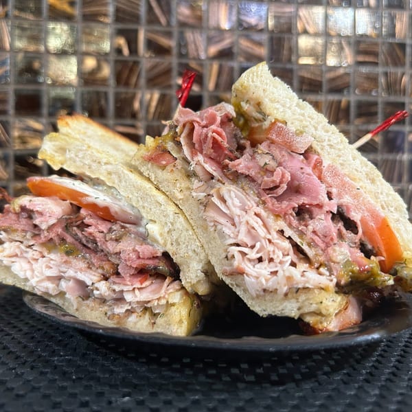 A deli sandwich, cut in half, revealing layers of meat, tomato, and sauce on toasted bread.