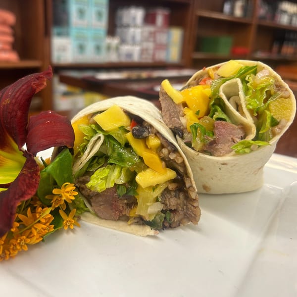 Two deli wraps filled with meat, lettuce, black beans, and mango salsa, garnished with flowers.