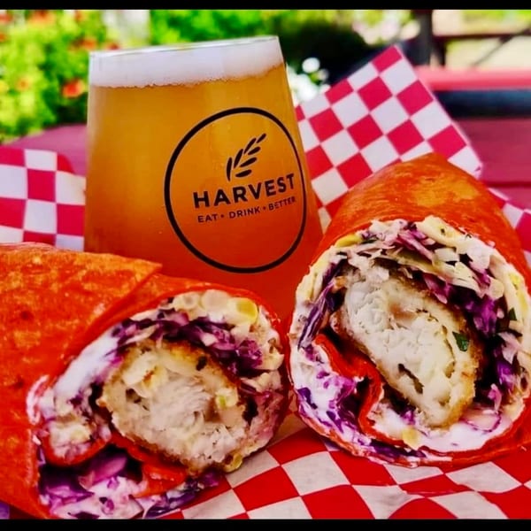 Two Harvest deli wraps with crispy chicken, red cabbage, and sauce, next to a beer.