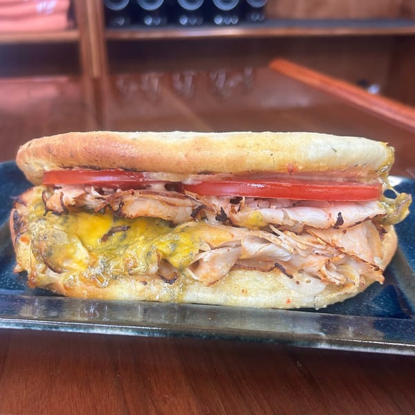 A Harvest deli sandwich with turkey, melted cheese, and sliced tomatoes on a dark plate.