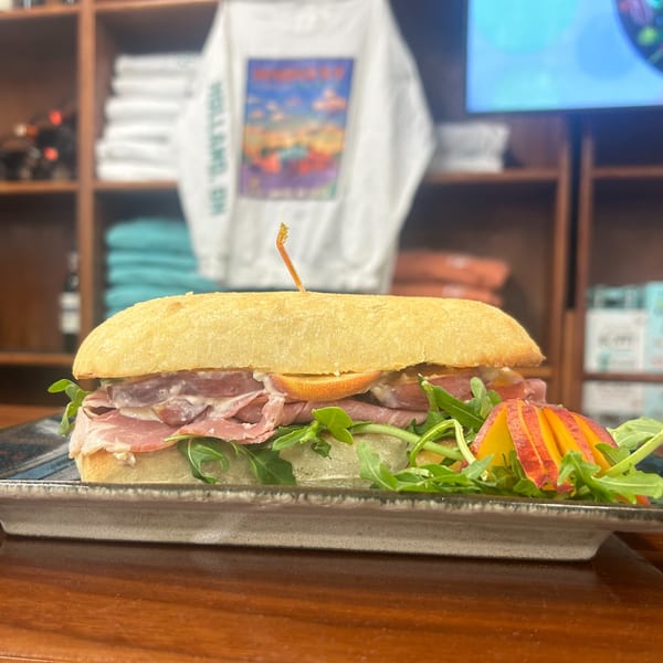 A Harvest deli sandwich with prosciutto, arugula, and sliced peaches on a ciabatta roll.
